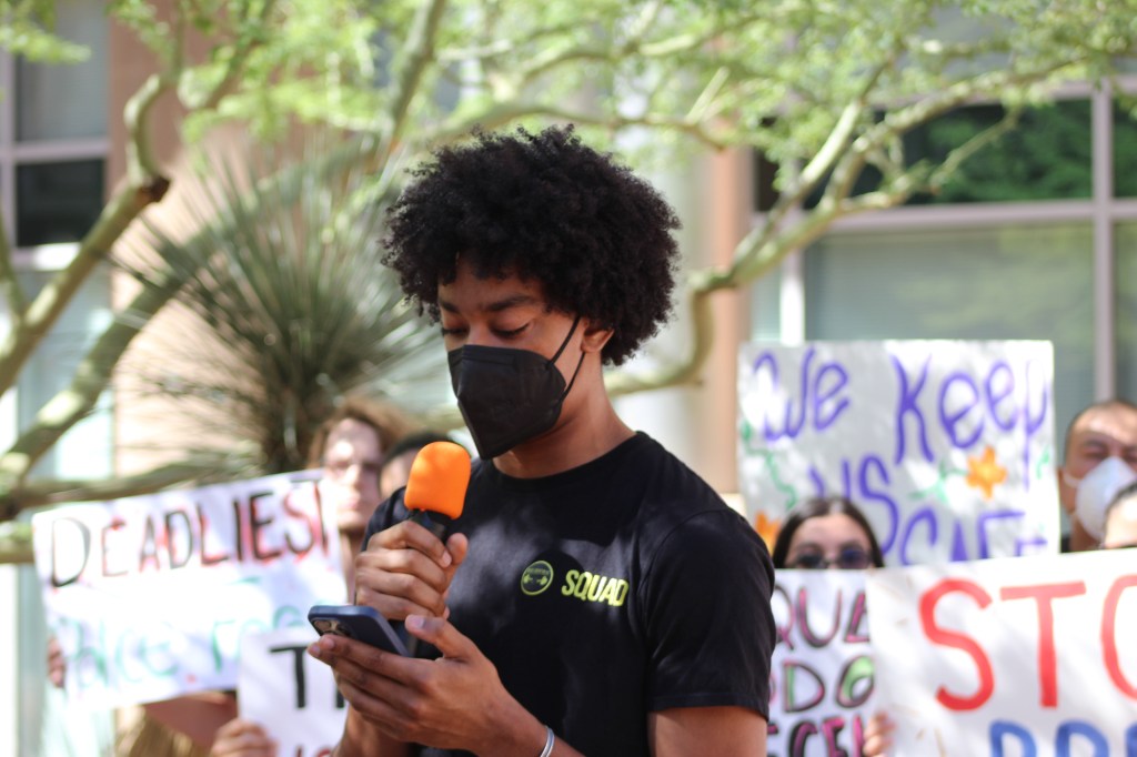 a man in a face mask speaks into a microphone at a protest