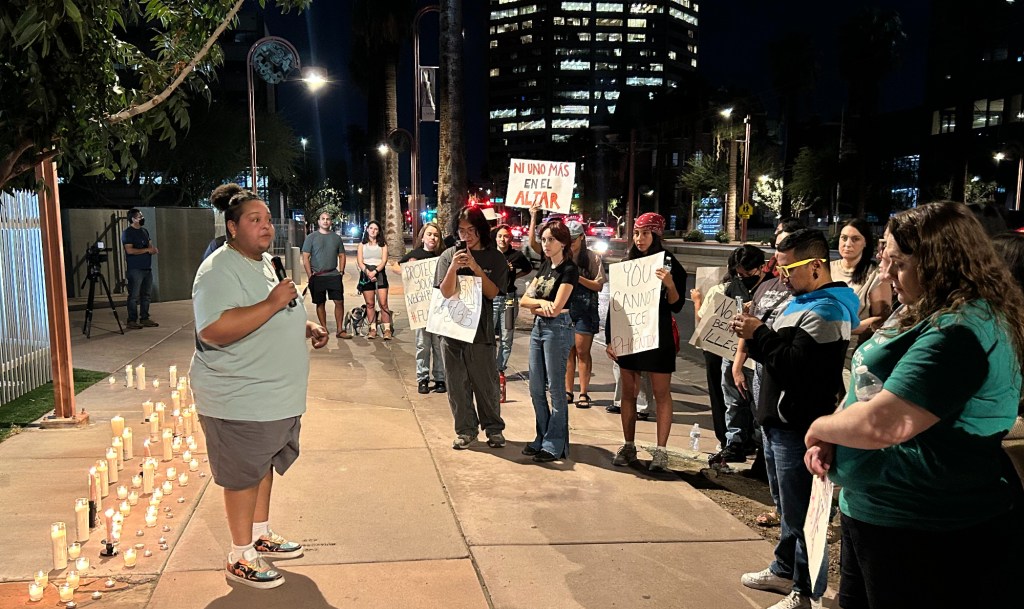 an activist speaks to a small crowd on a city street in front of dozens of candles