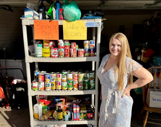 A woman stands next to a shelf of canned goods.