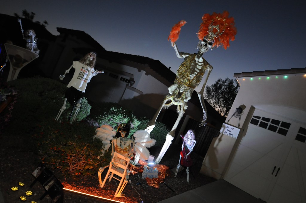 Skeletons dressed up as Taylor Swift outside a home at night.
