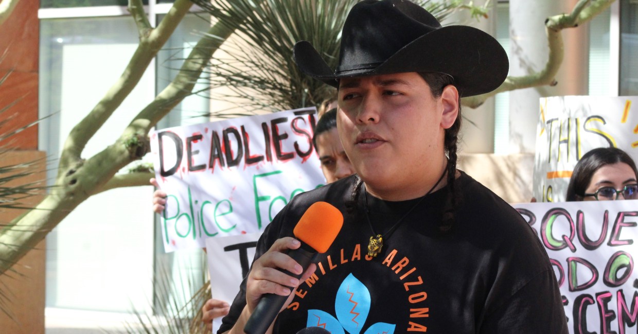 a man in braids and a cowboy hat speaks into a microphone
