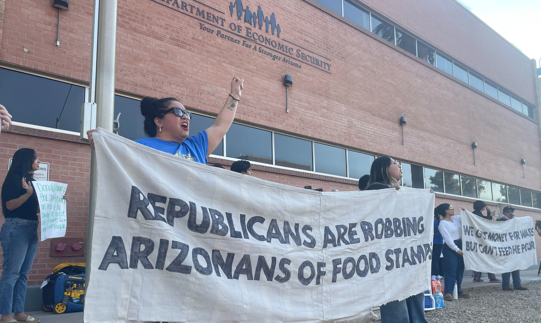 protesters hold a banner that says "republicans are robbing arizonans of food stamps"