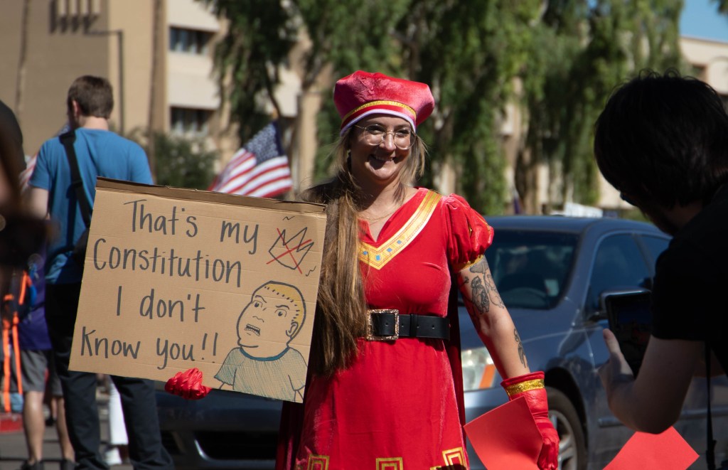 a protester holds a sign featuring the king of the hill character bobby hill and the caption "that's my constitution, i don't know you"