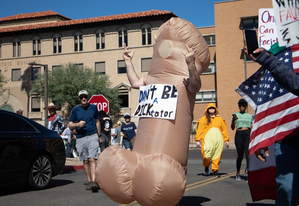 a protester dresses as a penis and holds an anti-trump sign