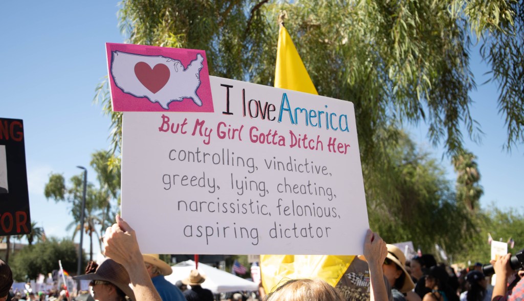 a protester holds a sign begging the U.S. to break up with trump