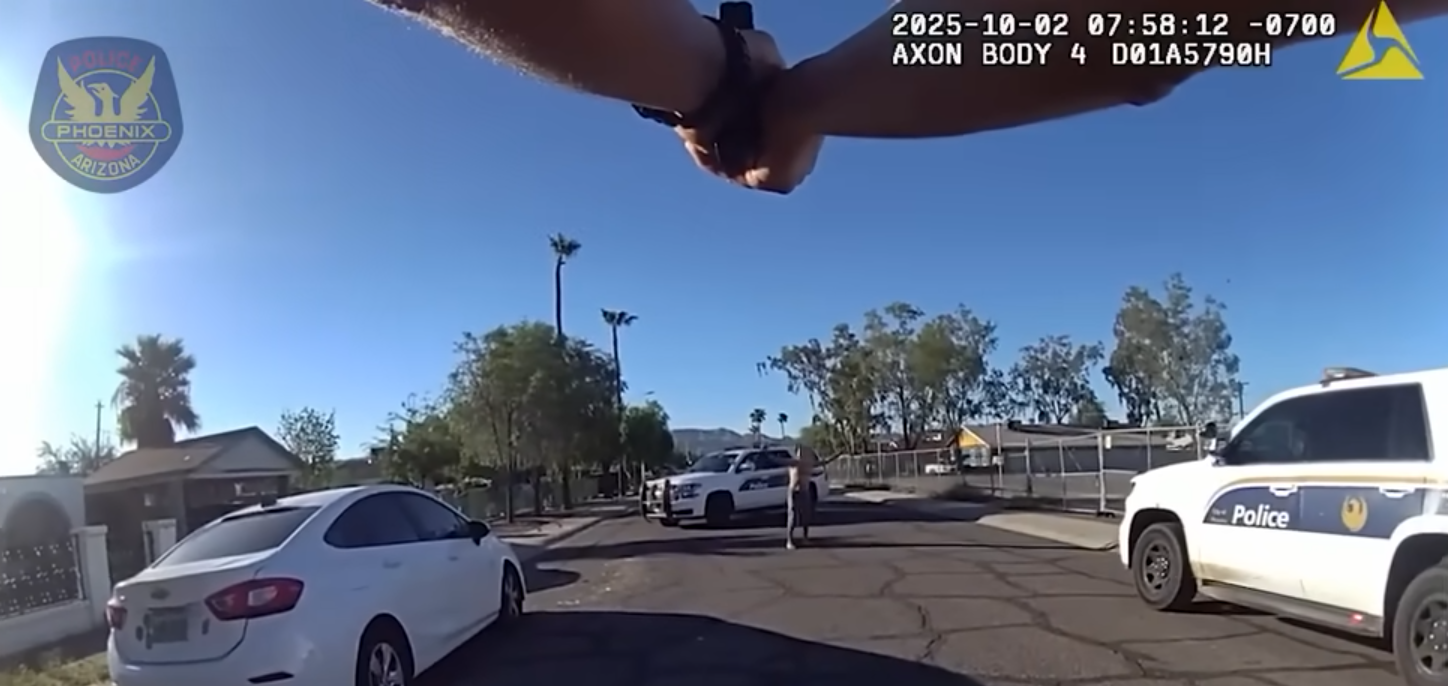 body-cam footage of someone pointing a gun at a shirtless man holding his hands up in the distance