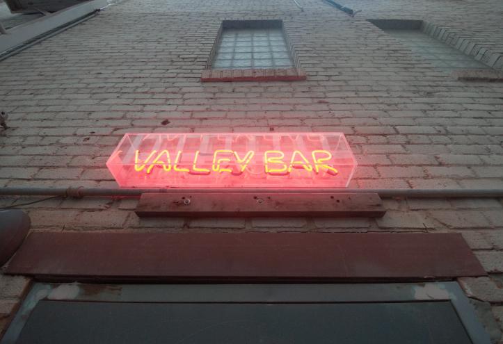 A neon sign on a brick wall above a door.
