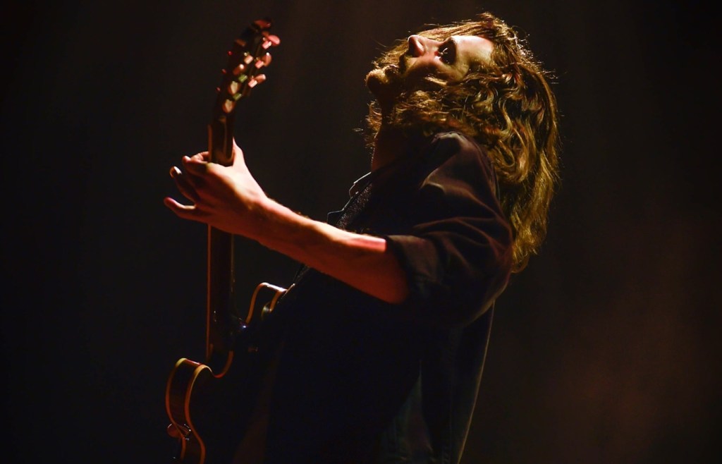 Long-haired musician tilts his head back while playing a guitar.