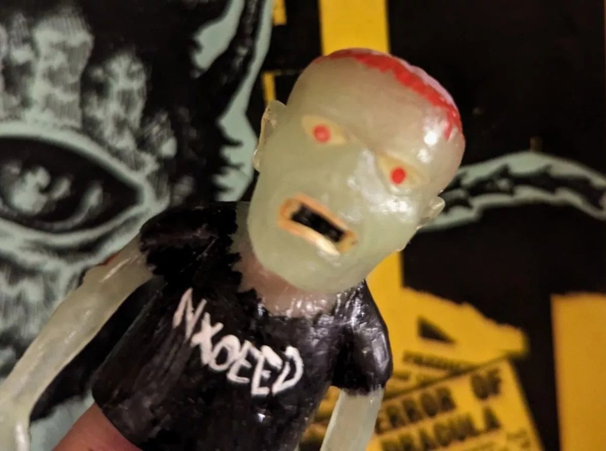 A ghoulish translucent action figure in a black t-shirt with the text "NXOEED" on it.