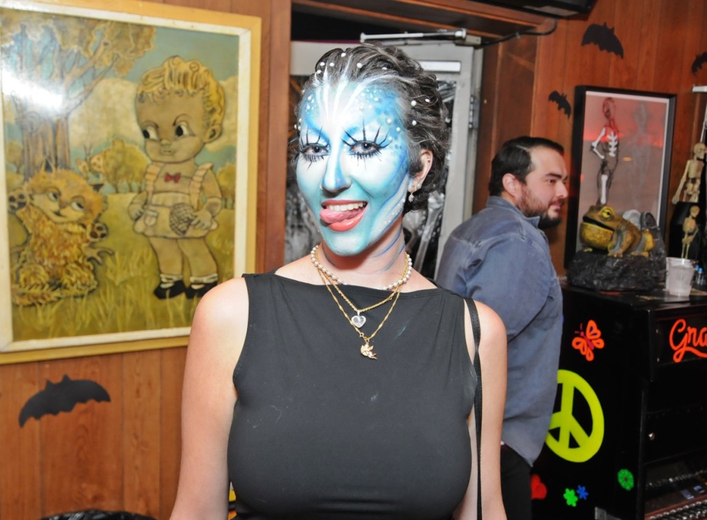 A woman in siren facepaint stands in a bar.
