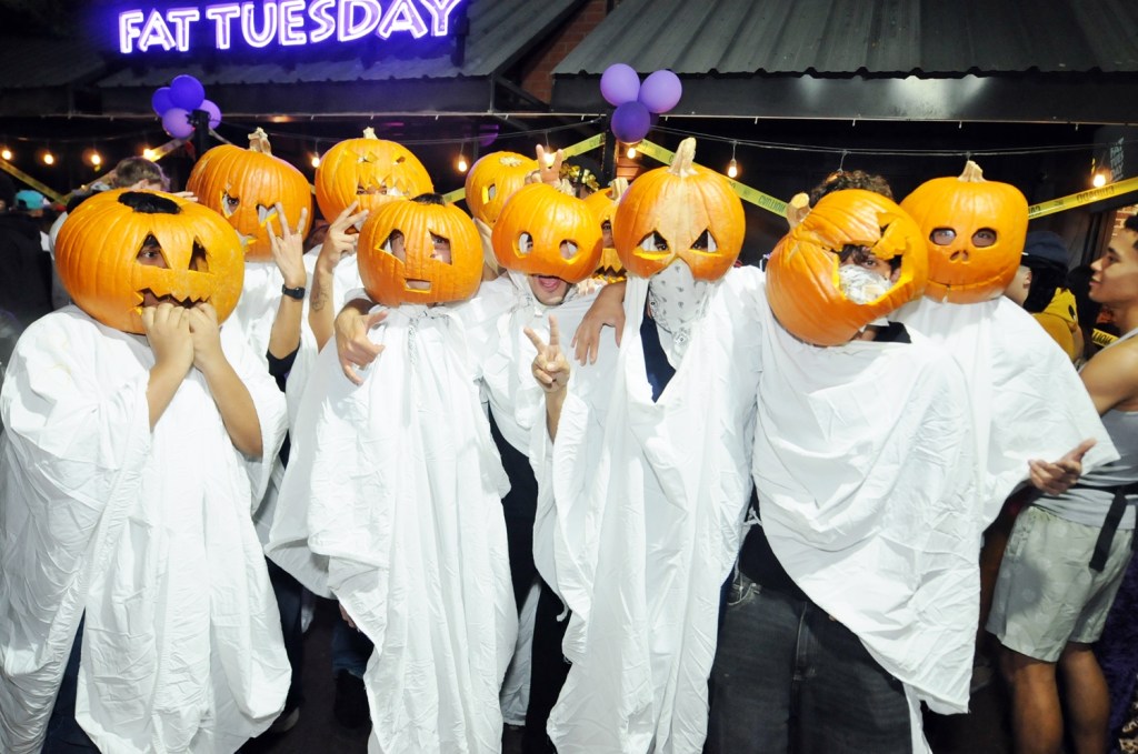 A group of nine men wearing pumpkins as masks outside a nightclub.