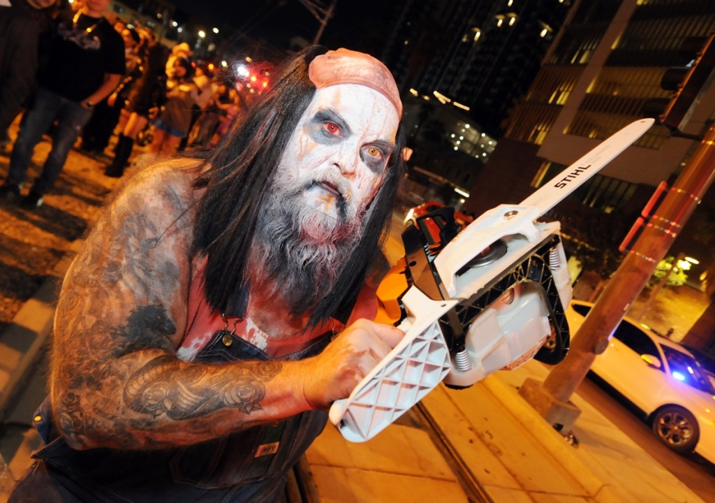 A man in clown makeup holds a chainsaw.