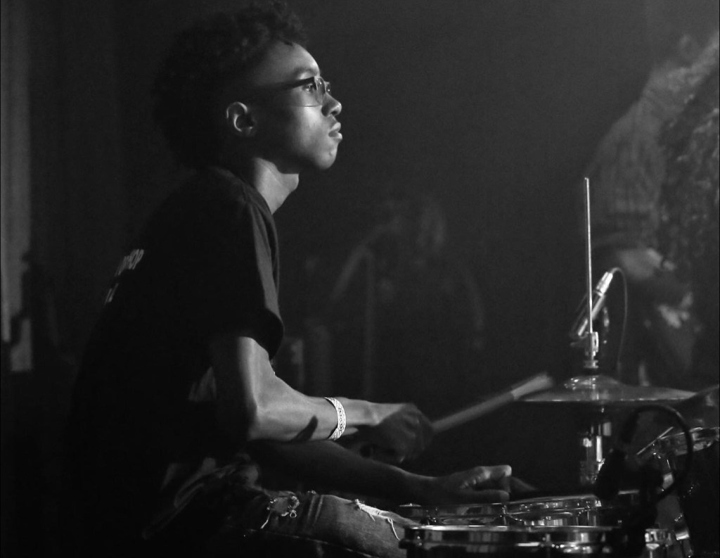An African-American youth sitting behind a drum kit.