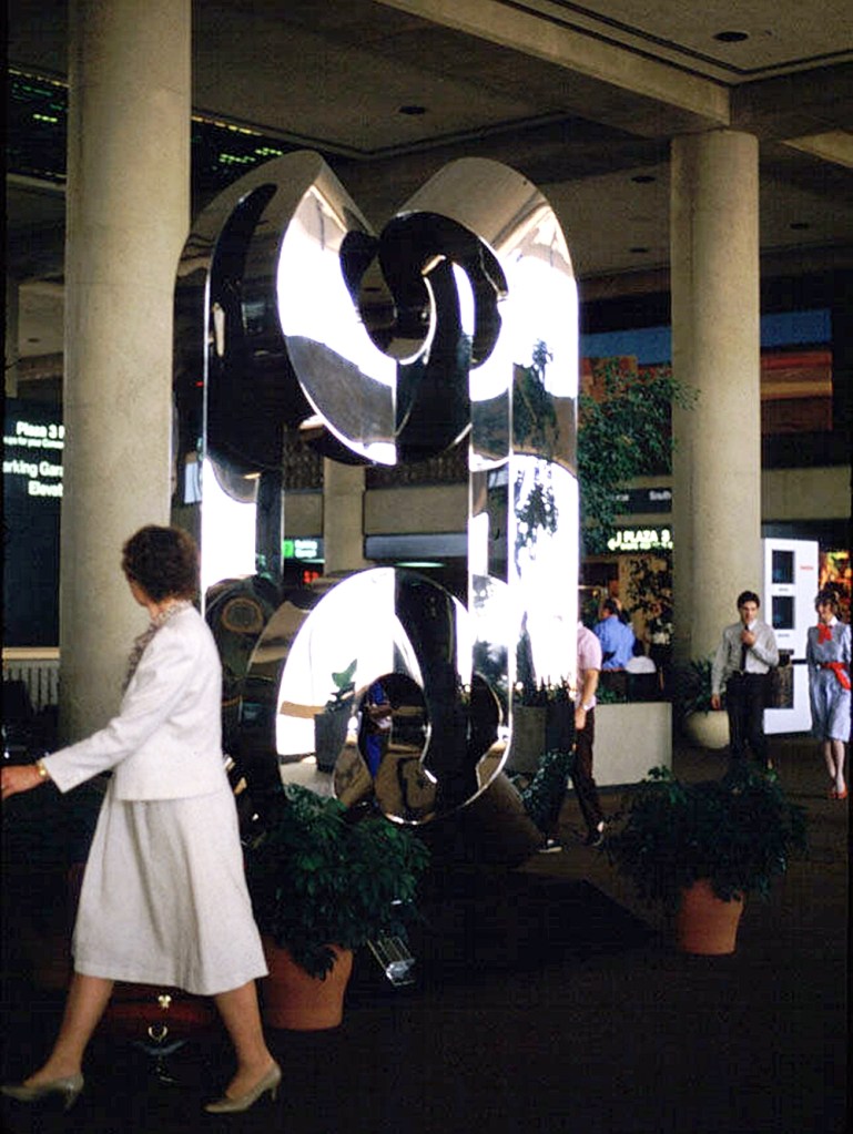 A silver modern art metal sculpture inside an airport terminal.