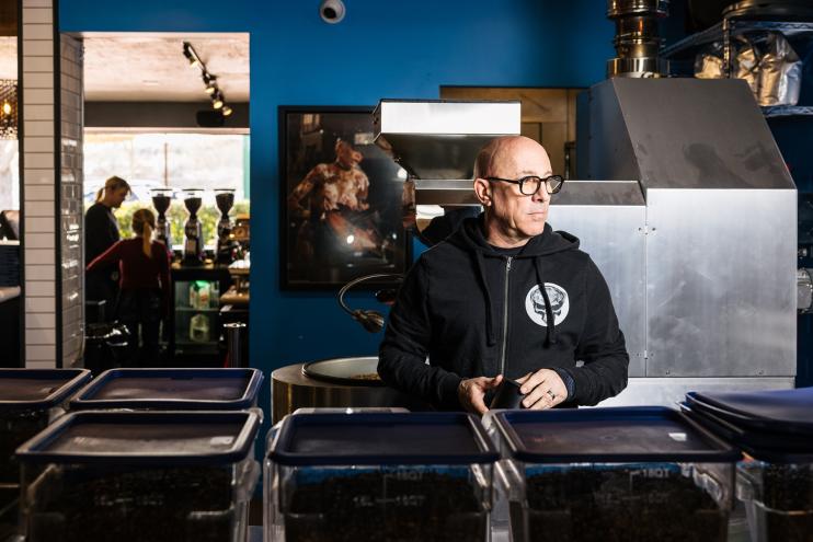 Bald man standing at a coffehouse counter.