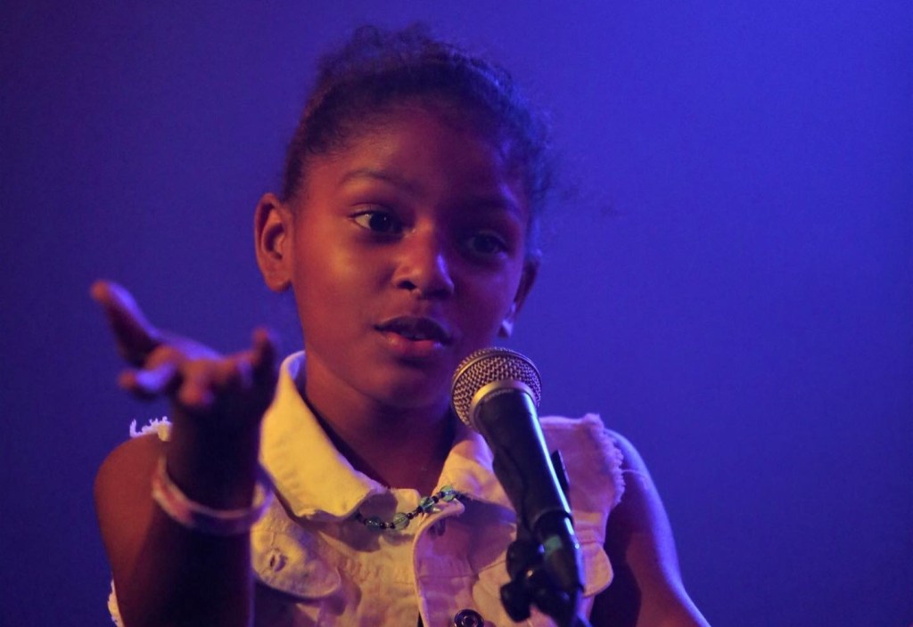A female African-American child sings into a microphone.