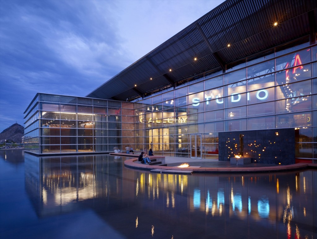 A glass and steel building facing a water feature at sunset.