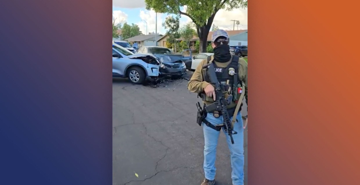 a masked ICE officer stands in front of two vehicles that have smashed into each other
