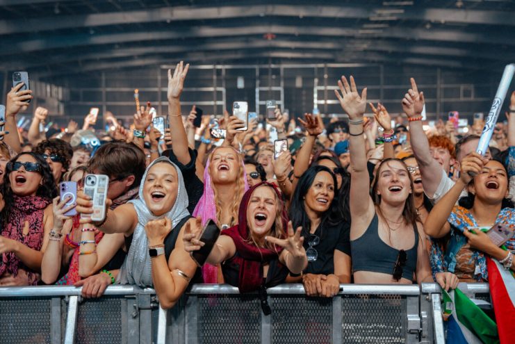 A huge crowd of people stand behind a security barrier at a music festival.