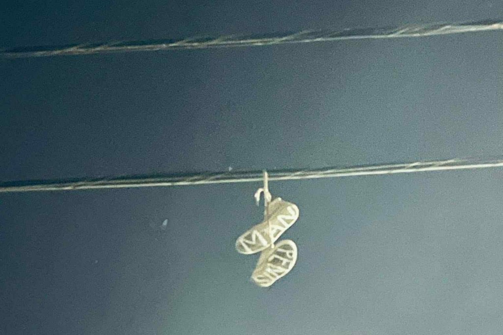 An old pair of shoes with the words "PENIS MAN" on the soles hanging from a utility wire.