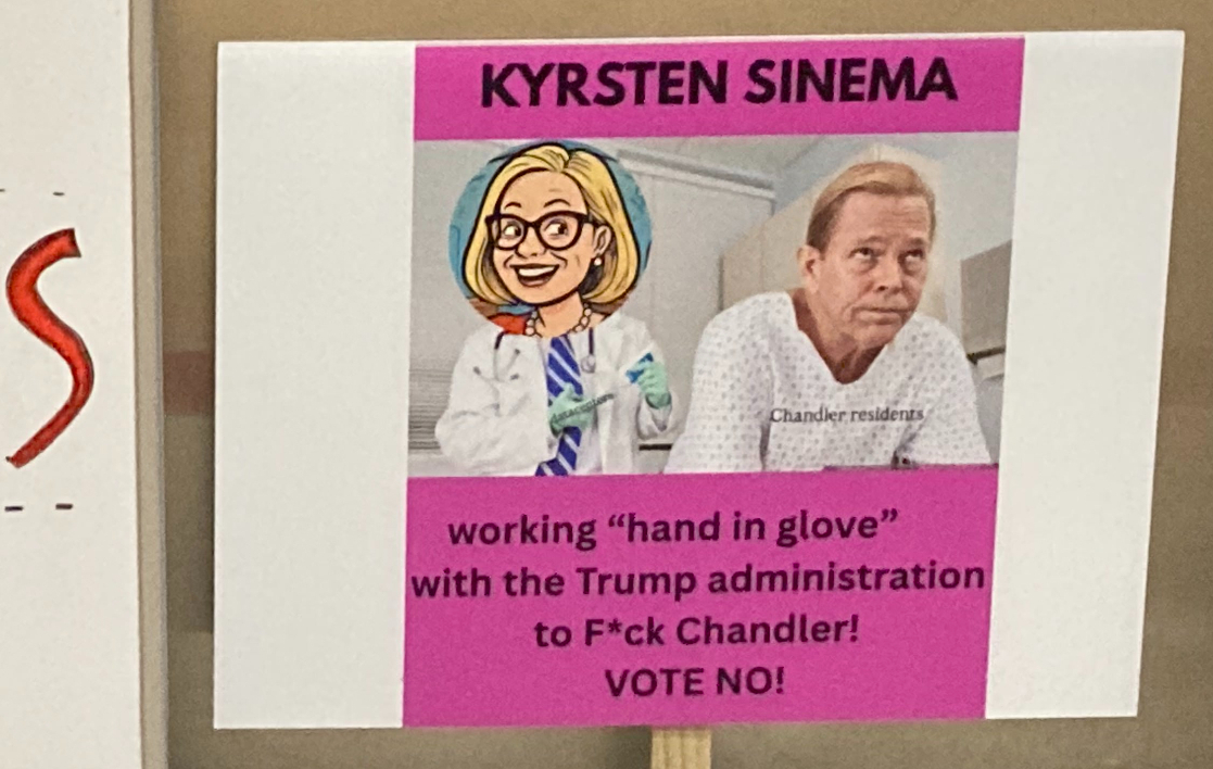 a sign showing kyrsten sinema putting on a rubber glove as a man labeled "chandler residents" bends over