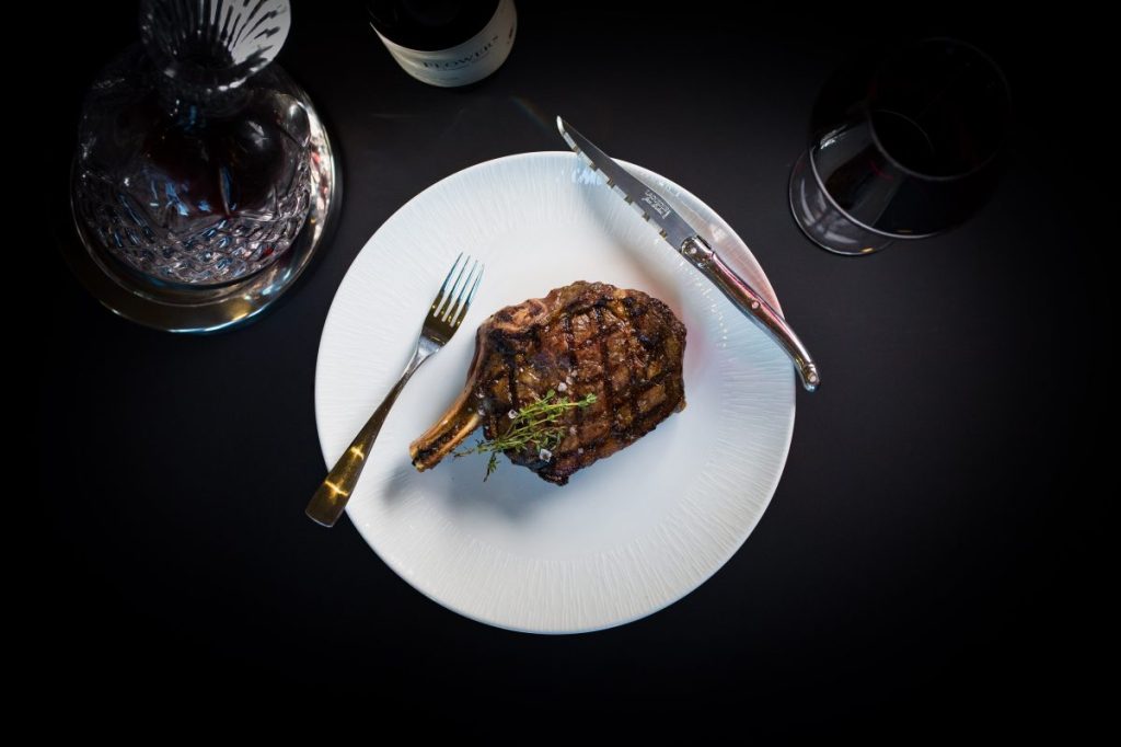 A steak on a plate next to a glass of wine.