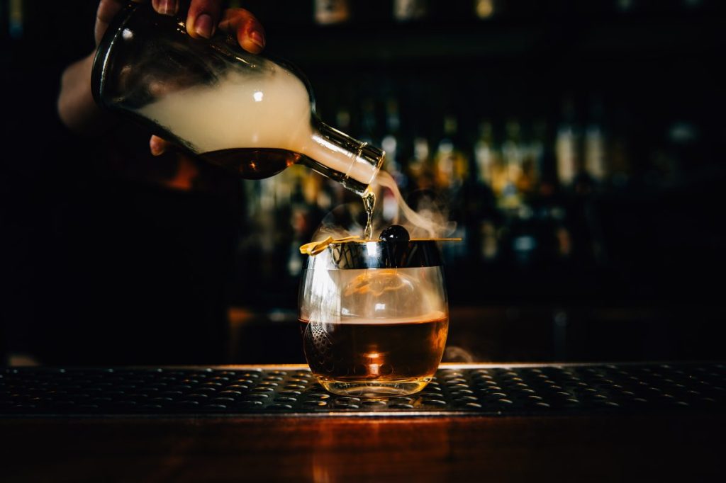 Pouring a smoked cocktail into a rocks glass at a bar.