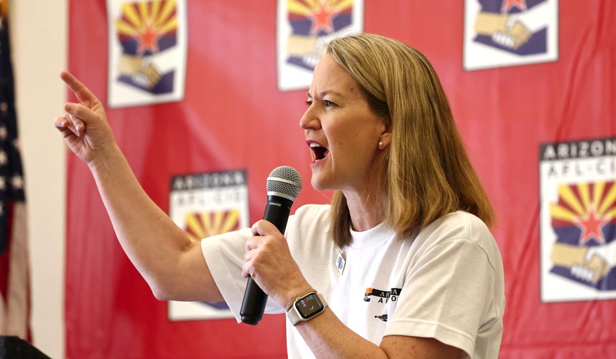 kris mayes points while holding a microphone