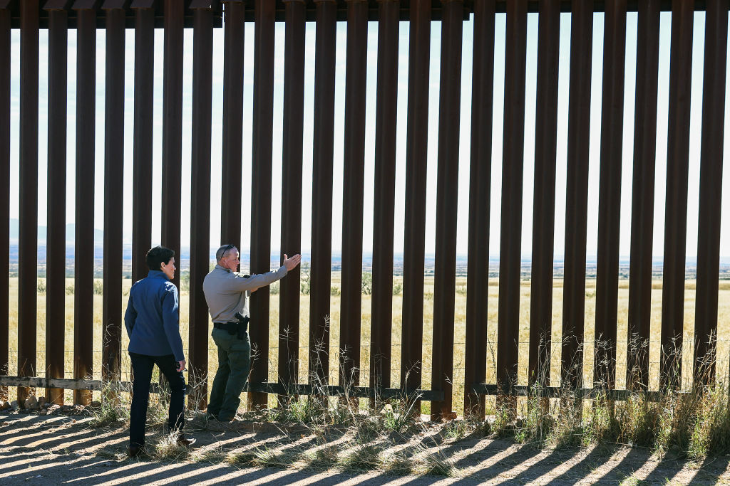 two people stand against a border wall