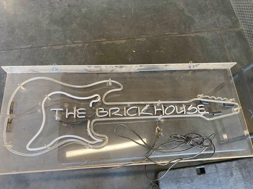 A non-functional neon sign in the shape of a guitar with the words "The Brickhouse" on the bridge,