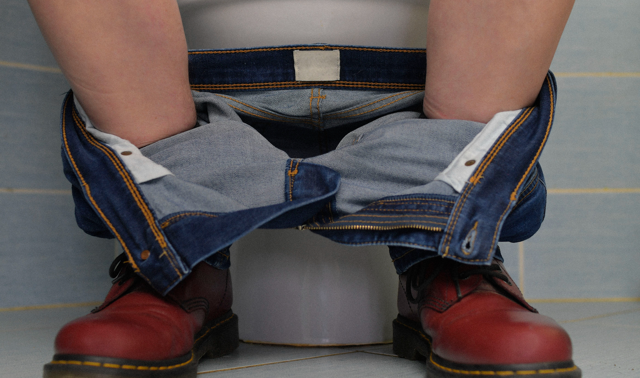 legs seen sitting on a toilet, with jeans down around the ankles