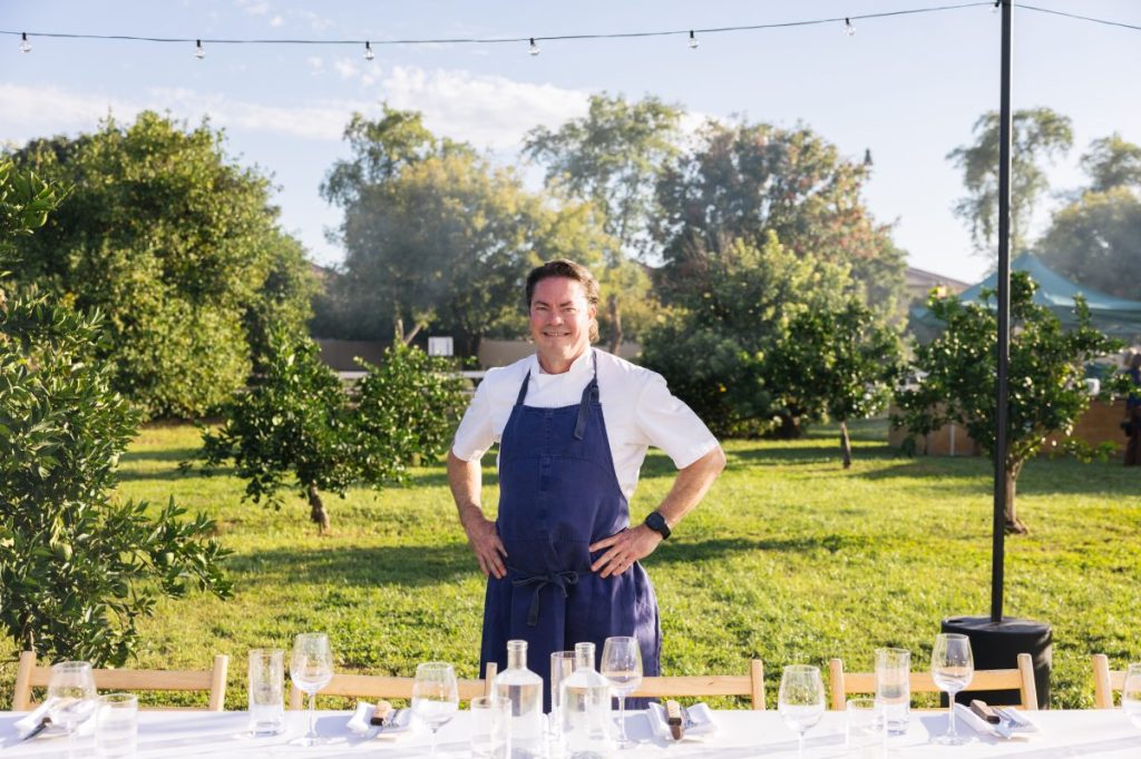 A chef standing in front of a dinner table set up at a farm.
