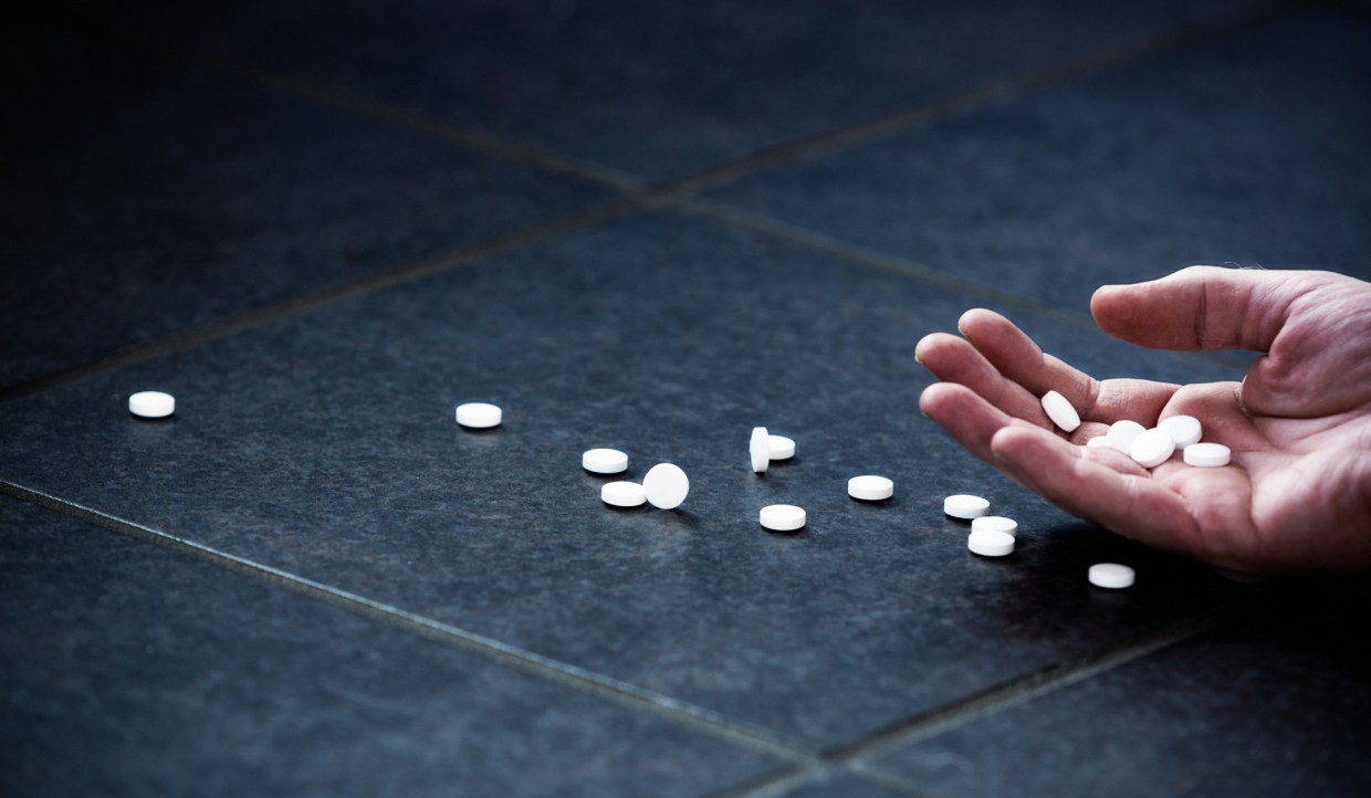 an empty hand lays on the ground as pills scatter around