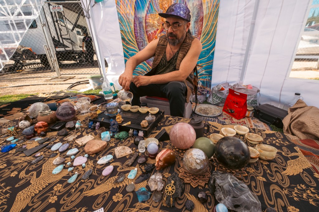 a man in a vest sits among an array of peculiar gemstones on a blanket