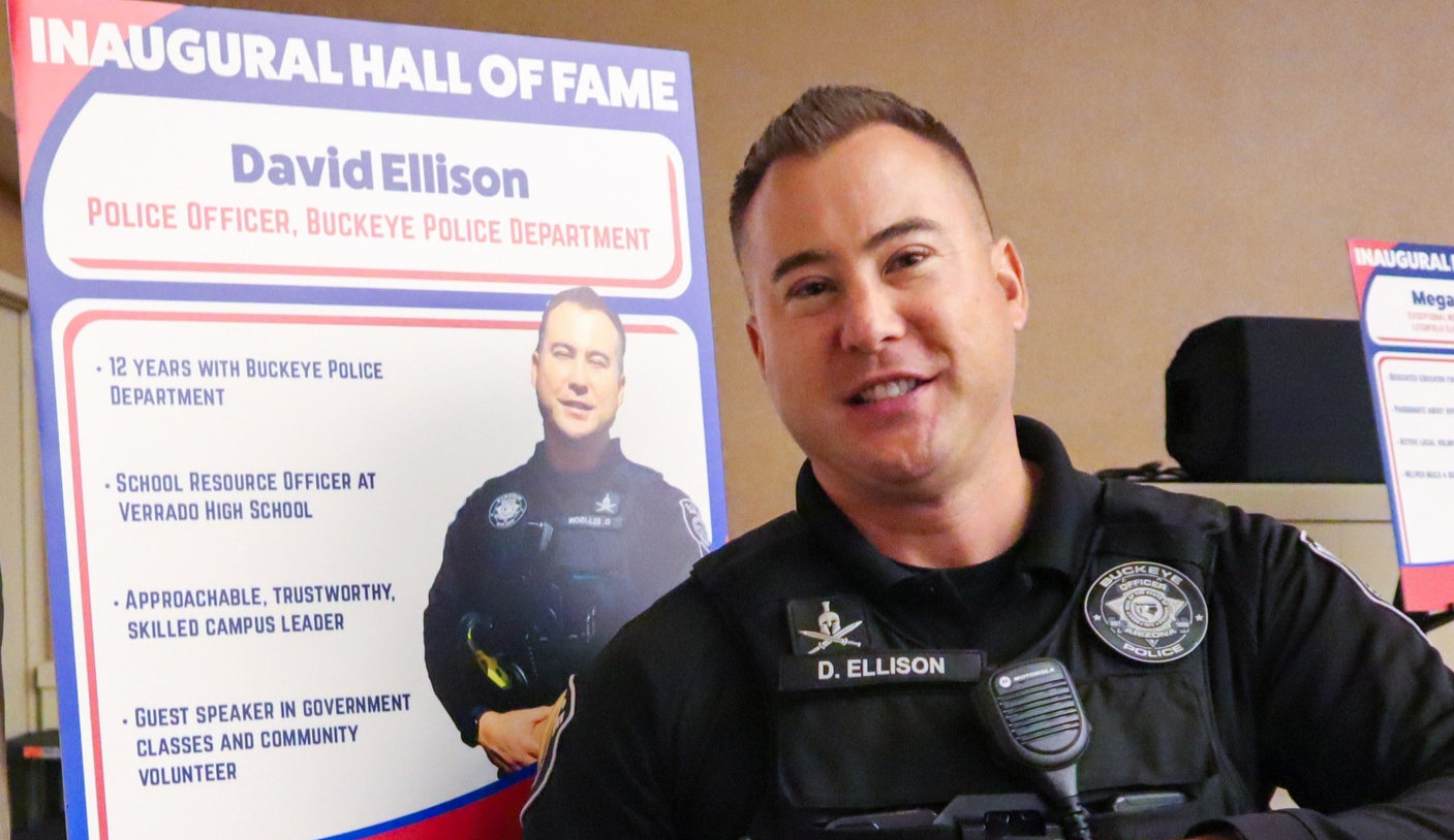 buckeye police officer david ellison in front of a placard celebrating his service to verrado high school