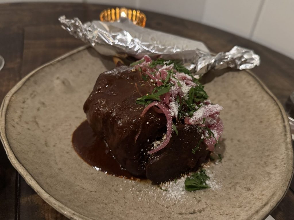 A pork shank platter, sauced in mole and topped with cotija, pickled onions and cilantro.