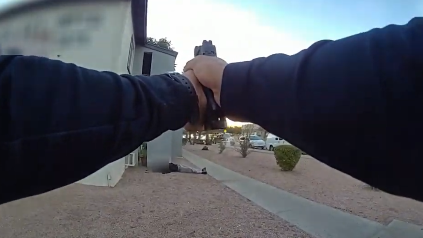 a still from a police officer's body camera showing two hands pointing a handgun at a man on the ground