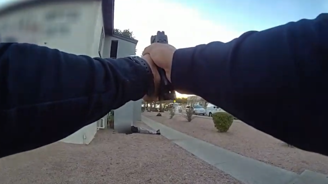 a still from a police officer's body camera showing two hands pointing a handgun at a man on the ground