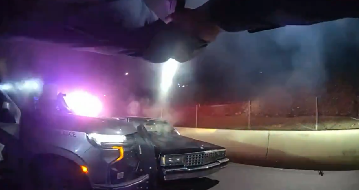 a still from body-cam footage showing someone pointing a handgun at a black car at night