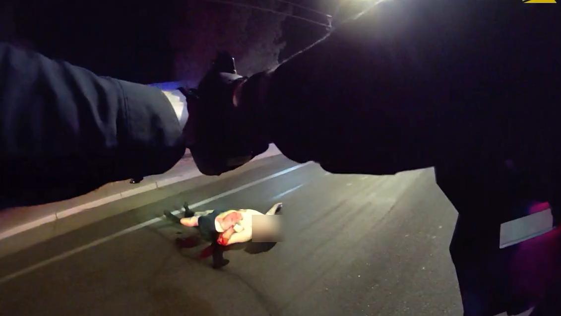 a body-worn camera still showing the arms of an officer pointing a gun at a shirtless man on the ground
