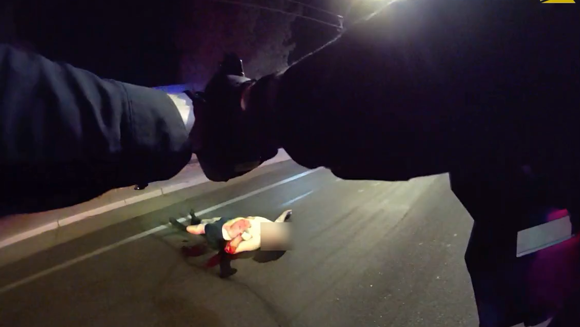 a body-worn camera still showing the arms of an officer pointing a gun at a shirtless man on the ground