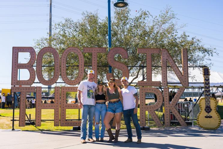 Three people pose in front of a "Boots in the Park" sign at Tempe Beach Park.