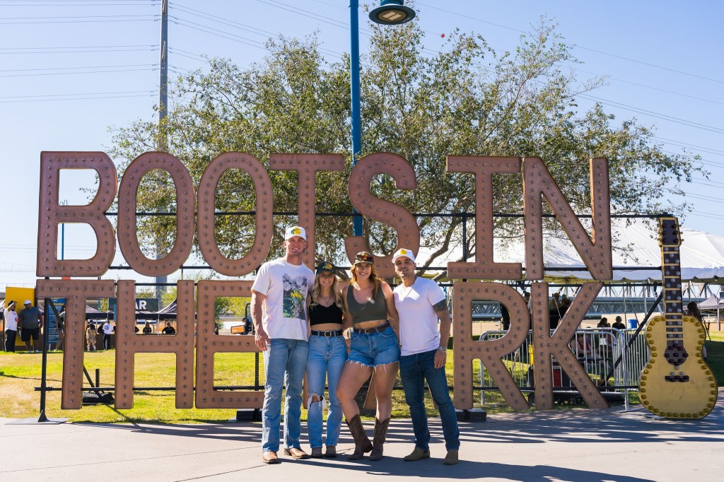 Three people pose in front of a "Boots in the Park" sign at Tempe Beach Park.