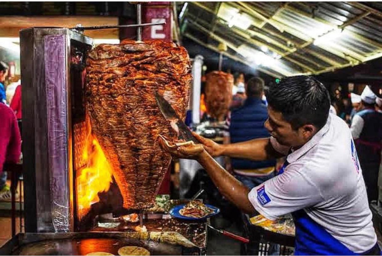 A chef carves al pastor off a cone of meat on a trompo.