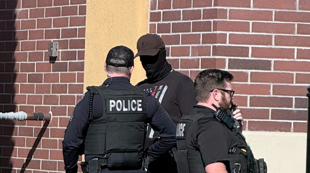 two police officers speak to a masked man near a building
