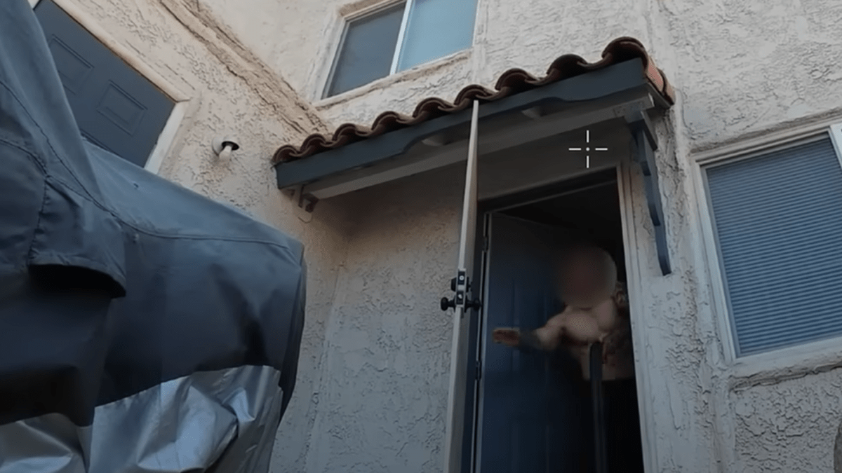 a shirtless man leans out a back door holding a long gun