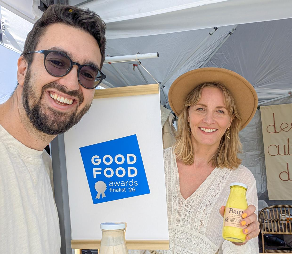 Two people holding Butta drinks at a farmers market booth.