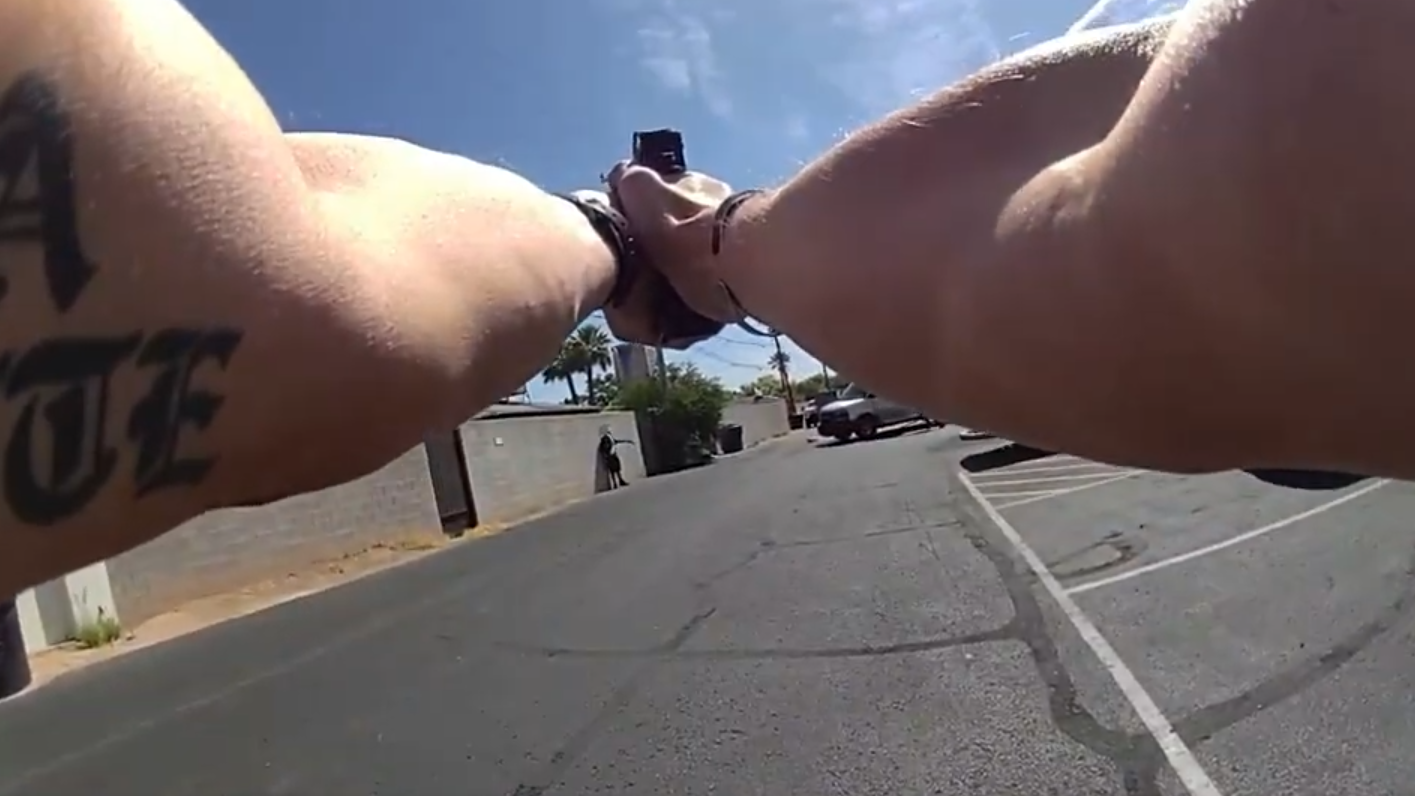 a body-cam footage still showing a police officer's arm pointing a gun at a man in an alley