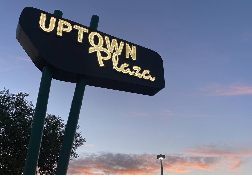 The neon Uptown Plaza sign glows against a colorful sunset sky along Camelback Road in Phoenix.