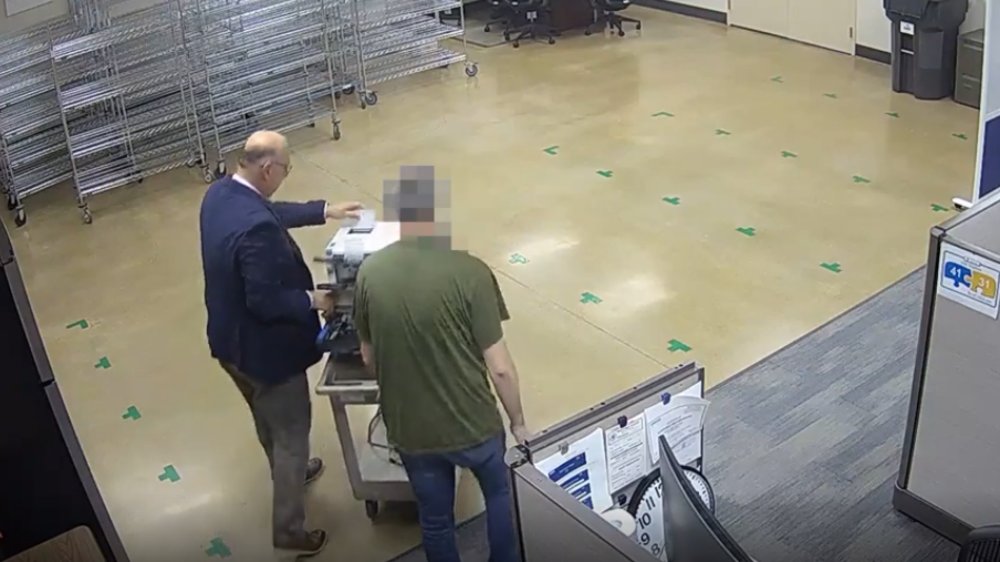 a security cam still showing bryan colby and another person wheeling a scanner through a room